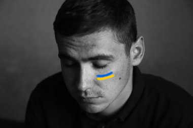 Genç Ukraynalı adamın Defocus portresi. Akıl sağlığı. Genç adam üzgün, ciddi, sorunları ve depresyonu var. Psikoloji konsepti. Stres ve acı. Gözleri kapalı. Yanağında Ukrayna bayrağı var. Odaklanamıyorum