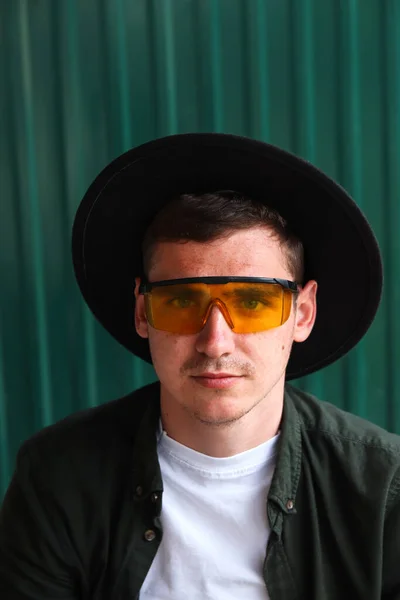Happy fashion man. Portrait of handsome smiling stylish hipster lambersexual model. Man dressed in yellow sunglasses and black hat. Fashion male on the modern background. Stylish people. Boy. 20s.