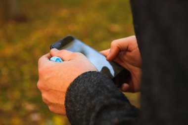 Defocus erkeği telefonu tutuyor. Sonbahar parkında akıllı telefon kullanan bir adam. Mesaj yazmak ya da cep telefonunda sosyal medya okumak. Arka planda kal. Cep telefonu. İletişim. Doğa. Odaklanamıyorum.