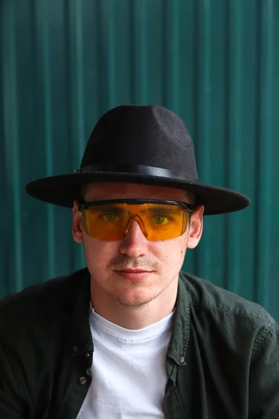 Happy fashion man. Portrait of handsome smiling stylish hipster lambersexual model. Man dressed in yellow sunglasses and black hat. Fashion male on the modern background. Caucasian. Guy. Boy.