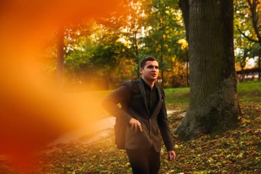 Sonbahar arka planında genç bir adamın portresi. Ciddi bir genç adam. 20 'li yıllar. Dışarıdaki yakışıklı adam portresi. Turuncu renkli. Parkta yürüyordum. Cep..