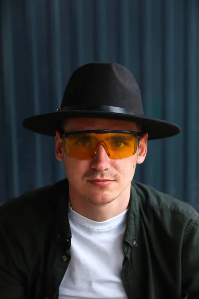 Happy fashion man. Portrait of handsome smiling stylish hipster lambersexual model. Man dressed in yellow sunglasses and black hat. Fashion male on the modern background. Caucasian. Guy.