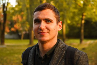 Sonbahar arkaplanındaki genç adamın Defocus portresi. Gülümseyen genç adam. 20 'li yıllar. Dışarıdaki yakışıklı adam portresi. Parkta yürüyordum. Yaşam tarzı. Odaklanamıyorum.