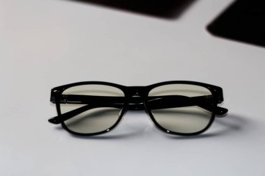 Defocus black eyeglasses on white background. Flat lay, top view. A pair of dark-rimmed glasses viewed from the front, with the temples open. Myopia. Chameleon glasses. Hipster eyewear. Out of focus.