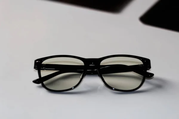 Defocus black eyeglasses on white background. Flat lay, top view. A pair of dark-rimmed glasses viewed from the front, with the temples open. Myopia. Chameleon glasses. Hipster eyewear. Out of focus.