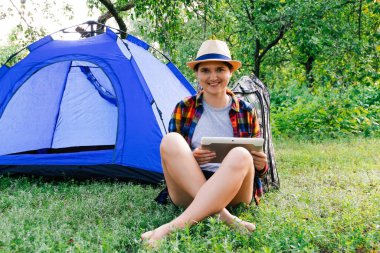 Dışardaki kamp çadırının yanında tablet üzerinde çalışan genç bir kadın güzel doğayla çevrili. Serbest çalışma, ücretli izin, akıl sağlığı. Odaklanamıyorum.