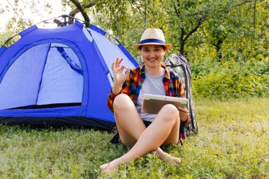 Dışardaki kamp çadırının yanında tablet üzerinde çalışan genç bir kadın güzel doğayla çevrili. Serbest çalışma, ücretli izin, akıl sağlığı. Tamam jest. Odaklanamıyorum.