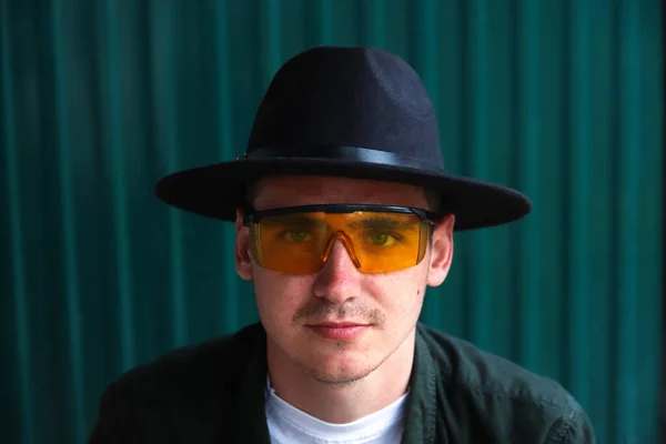 Happy fashion man. Portrait of handsome smiling stylish hipster lambersexual model. Man dressed in yellow sunglasses and black hat. Fashion male on the modern background. Caucasian.