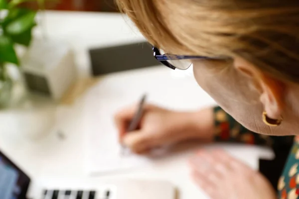 Defocus female hand writing pen. Unrecognizable elegant woman working on computer at office. Start or finish of a work day. Workspace. Top view. Time for work. Closeup businesswoman. Out of focus.