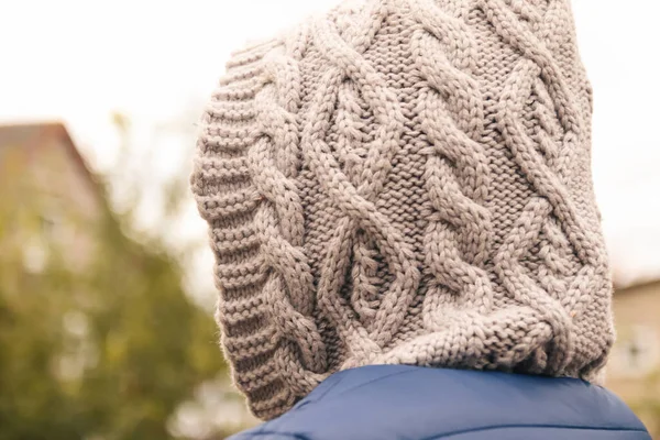 Defocus knitted hood outside, back view. Closeup. Young woman in a hood stands with her back to the camera on a background. Out of focus.