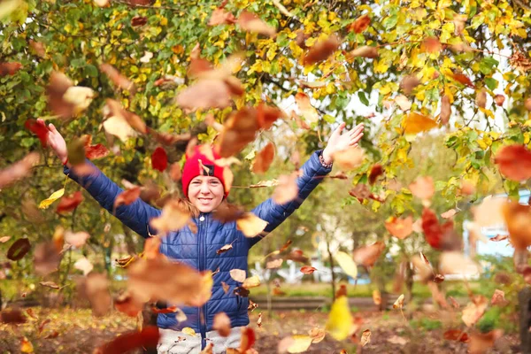 Defocus autumn people. Teen girl raising hand and throwing leaves. Many flying orange, yellow, green dry leaves. Enjoy autumn. Happy fall. Funny season. Smiling child. Out of focus.