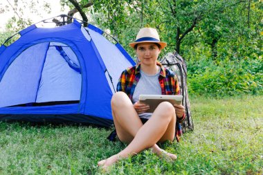 Dışardaki kamp çadırının yanında tablet üzerinde çalışan genç bir kadın güzel doğayla çevrili. Serbest çalışıyorum. Odaklanamıyorum.