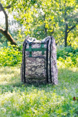 Askeri sırt çantasından çık. Ağacın yanındaki yeşil çimlerin üzerinde ordu çantası. İngiliz ordusunun sırt çantasında askeri kamuflaj malzemesi. Dikey. Turist yaz yürüyüşçüsü. Trip konsepti. Odaklanamıyorum.