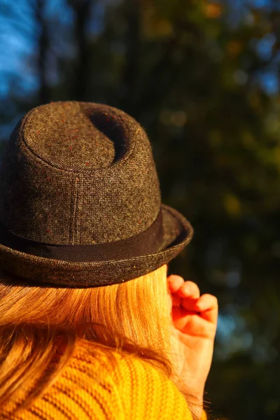 Defocus closeup back portrait of candid young Caucasian blonde woman in colorful autumn park. Bright dark stylish woman in hat. Happy fall dreaming waiting concept. Out of focus.