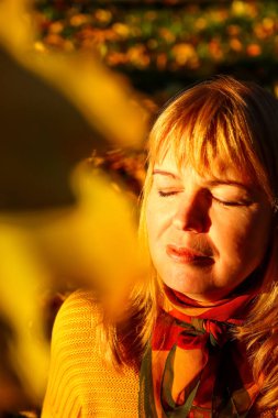Defocus closeup portrait of candid young Caucasian blonde woman in colorful autumn park. Bright stylish woman in yellow pullover and shawl of neck on fall background. Happy fall. Out of focus.
