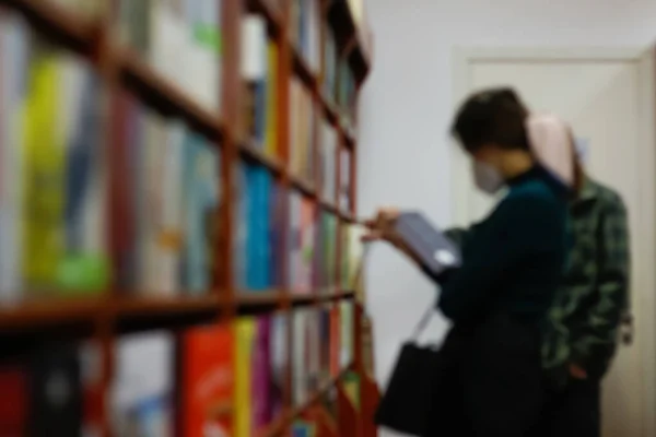Defocus reading concept. Vintage tone of woman selecting book from a bookshelf. Portrait of girl in library reading book Female hand holding a book in library, study, education. Bookshop Out of focus.