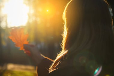 Defocus silhouette side view of smiling woman looking at oak tree leaf. Mental health, hope, happiness concept. Dream autumn. Peace lifestyle. Sunlight in fall park or forest. Out of focus.