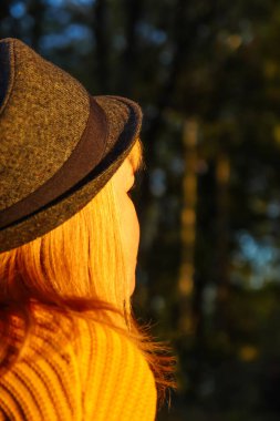 Defocus closeup back portrait of candid young Caucasian blonde woman in colorful autumn park. Bright dark stylish woman in hat on fall background. Happy fall dreaming waiting concept. Out of focus.