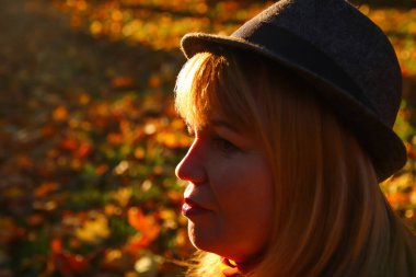 Defocus closeup portrait of smiling young Caucasian blonde woman in colorful autumn park. Bright stylish woman in hat on orange fall background. Happy fall dreaming concept. Out of focus.