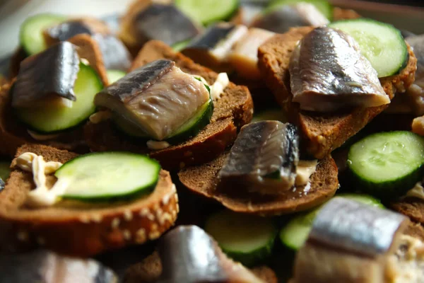 Defocus sandwich with herring and cucumber. A piece of black bread. Healthy food. Plate of sandwiches with fresh herring fish on dark background. Closeup. Out of focus.