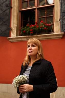 Kırmızı arka planda duran ve elinde beyaz çiçekler tutan defocus kadını. 40 'lı yaşlarda ciddi kadın. Uzayı kopyala Kadın portresi. Gelin grubu. Sarışın kadın. Odaklanamıyorum.