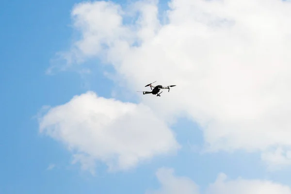 Defocus war drone. Drone flying in a blue sky. The black army unmanned aerial vehicle with four propellers and blades is on the blue sky background. White clouds. Out of focus.