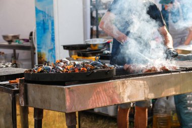 Dışardaki festivalde bbq eti pişiren defocus adamı. Deniz ürünleri paella 'sı. Şef dışarıda parkta sosis ızgara yapıyor. Aileler ve arkadaşlarla yaz partisi kavramı. Odaklanamıyorum.