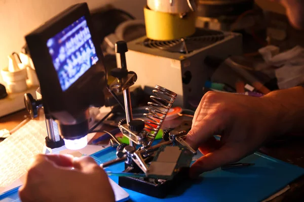 Defocus male hand with microscope. Work with a soldering iron. Microelectronics device. Close-up hands of a service worker repairing modern smartphone. Repair and service concept. Out of focus.