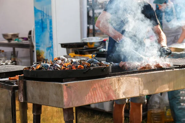 Dışardaki festivalde bbq eti pişiren defocus adamı. Deniz ürünleri paella 'sı. Şef dışarıda parkta sosis ızgara yapıyor. Aileler ve arkadaşlarla yaz partisi kavramı. Odaklanamıyorum.