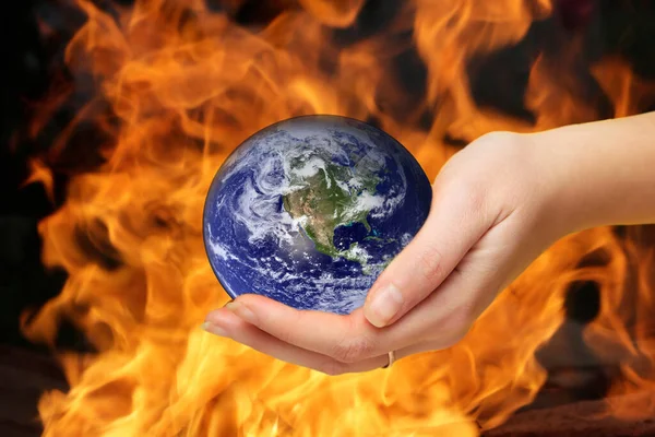 Defocus female hand holding planet globe on fire flame background. Environmental protection concept. Earth in hands. Save of Earth. Elements of this image furnished by NASA. Out of focus.