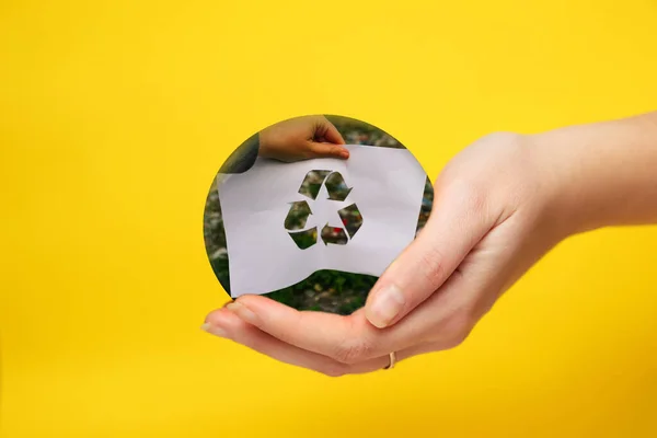 Defocus hand holding cut paper with the logo of recycling on dump garbage trash background. Yellow background. Recycling concept. Pollution of the planet. Out of focus.