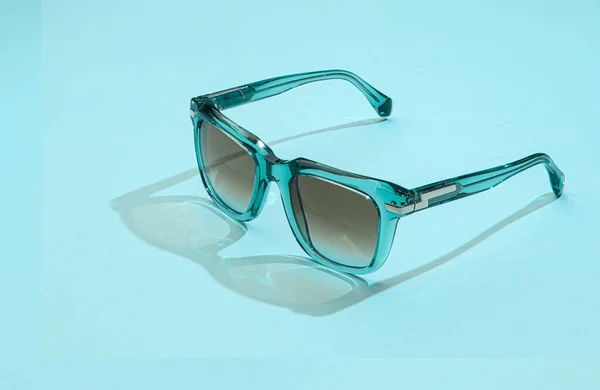 Nowoczesne okulary przeciwsłoneczne na pastelowym niebieskim tle. Okulary przeciwsłoneczne kobiety ze światłem słonecznym na wakacje koncepcji. — Zdjęcie stockowe