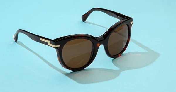 Moderní sluneční brýle na pastelově modrém pozadí. Sluneční brýle ženy se slunečním světlem pro letní dovolenou koncept. — Stock fotografie
