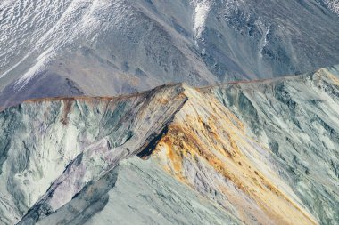 Karla kaplı dağ ve turuncu ve leylak renkli gri kayalıklarla kaplı çok renkli sonbahar manzarası. Sonbaharda keskin dağ sırtına muhteşem renkli bir manzara. Motley dağ manzarası Sonbahar renklerinde.