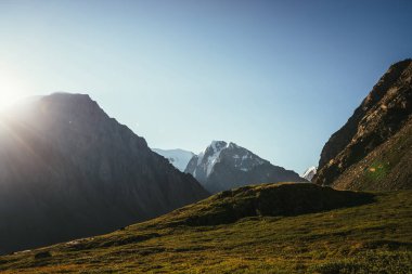 Yüksek karlı dağ zirvesine ve gün ışığında buzulun rengarenk manzarası. Güneş ışınları ve güneş patlamalarıyla güzel güneşli bir manzara. Karla kaplı büyük bir dağ tepesi olan canlı doğa manzarası. En düşük alp görünümü.
