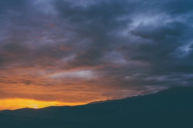 Atmosferik manzara. Dağların siluetleriyle. Ağaçların arka planında parlak turuncu mavi şafak gökyüzü. Günbatımının ya da aydınlatıcı rengin gün doğumunun olduğu renkli doğa manzarası. Günbatımı ödemesi