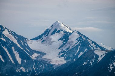 Bulutlu gökyüzünün altında, büyük, karlı dağ zirvesi mavi beyaz renklerle muhteşem dağlar. Atmosferik dağ manzarası, yüksek dağ duvarı, beyaz bulutların altında kar var..