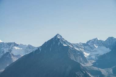 Atmosferik dağ manzarası. Siyah dağ silueti. Güneş ışığında karlı, keskin kayalık bir tepe noktası. Alp manzaralı, karla kaplı dağ tepede, mavi gökyüzünün altında gün ışığıyla tepede.