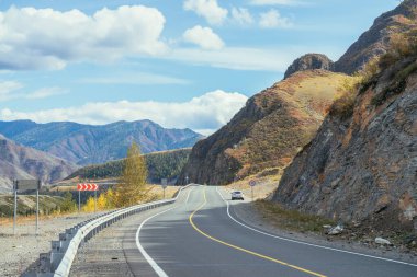 Dağ otobanındaki araba sonbahar renklerinde gün ışığında kayalar boyunca. Dağ yolu ile renkli bir manzara. Sonbahar zamanı dağlarda otoyol. Rusya, Altai Cumhuriyeti, Chuysky yolu, 19 Eylül 2020.
