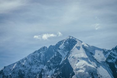 Büyük karlı dağ manzarası mavi beyaz renklerde ve mavi gökyüzünde beyaz sirrus bulutları. Atmosferik dağ manzarası, yüksek dağ duvarı ve sivri uçlu karla kaplı.