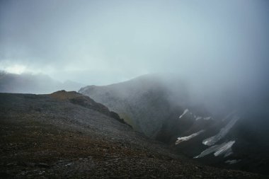 Dağlık bölgelerdeki uçurumun kenarındaki karanlık atmosferik manzara. Alçak bulutlar arasında tehlikeli dağlar ve uçurum. Tehlikeli dağ geçidi ve bulutlardaki keskin kayalar. Dağlarda tehlikeli bulutlu yağmurlu hava.