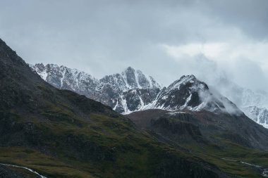 Atmosferik dağ manzarası alçak bulutlarda karla kaplı. Bulutlu havada keskin zirvesi olan dramatik dağ manzarası. Bulutlu gökyüzünde karlı, sivri tepeye müthiş bir manzara.