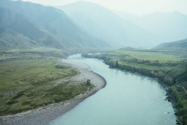 Geniş dağ nehri olan güzel sisli dağ manzarası. Koyu yeşil kasvetli manzara ve sisli dağ nehri. Yağmurlu havada, büyük dağların arasındaki büyük nehrin karanlık atmosferik görüntüsü.