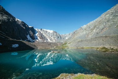 Karlı dağ, buzul gölünün berrak sularına yansıyor. Berrak gökyüzünün altındaki dağ gölünün su yüzeyinde buzul yansıması olan güzel güneşli bir manzara. Dağdaki gölde yansıyan karlar..