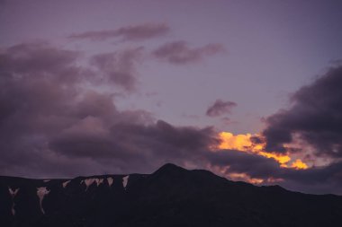 Atmosferik dağ manzarası, şafak vakti leylak rengi gökyüzü. Mor gün batımında gökyüzü altında kar olan kayalıklı manzara. Dağlarda, pastel tonlarda güzel bir gündoğumu. Şafak vakti bulutlu gökyüzünde aydınlatıcı bir renk.