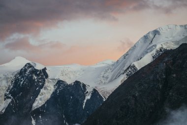 Gün batımının arka planında karlı dağ manzarası ya da turuncu renkli bulutlu gün doğumu bulutlu gökyüzü. Atmosferik dağlar. Turuncu şafak vakti gökyüzünde kar beyazı dağ sırtı..