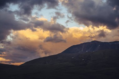 Bulutlu gökyüzünde altın şafak ışığıyla güzel bir dağ manzarası. Gün batımı gökyüzünde aydınlatıcı renklere sahip manzaralı dağ manzarası. Gün doğumunda dağların siluetleri. Gökyüzünde aydınlatan altın rengi güneş ışığı