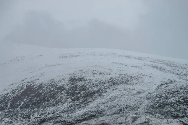 曇りの空に黒い岩の上に白い雪と霧の山の風景 低雲の中に雪に覆われた山の頂上の霧の山のミニマリスト 霧の中で雪の山のピークの最小限の自然背景 — ストック写真
