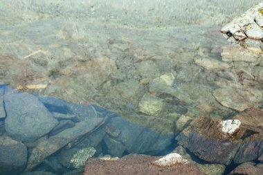 Güneş ışığında, buzul gölünün şeffaf sularında taş zeminin güzel doğa arka planı. Buzul gölünün berrak sularında pek çok taş bulunan güneşli bir zemin. Dağ gölünün görünmez suyu.