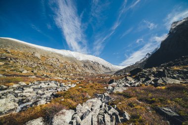 Sonbahar güneşli manzarası Highland Vadisi ve karla kaplı dağ sıraları sirrus bulutlu mavi bulutlu gökyüzü altında. Sonbaharda kayalık dağların arasında güneşli vadiyle güzel dağ manzarası